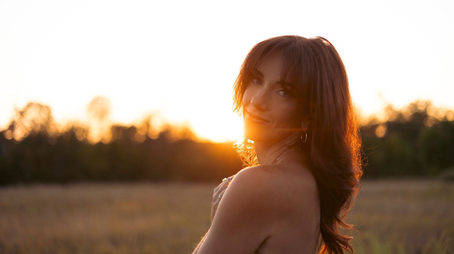 A silhouetted figure walks through a golden field at sunset with a warm orange glow in the background.
