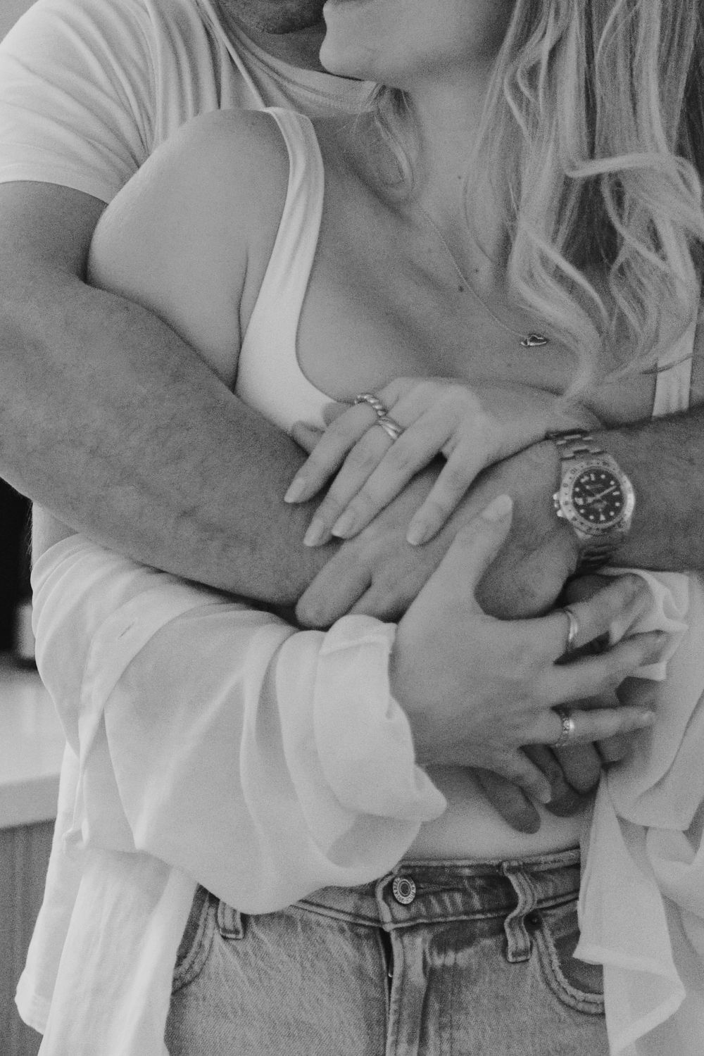 A tender black and white close-up shows embracing couple with hands intertwined and a watch visible.