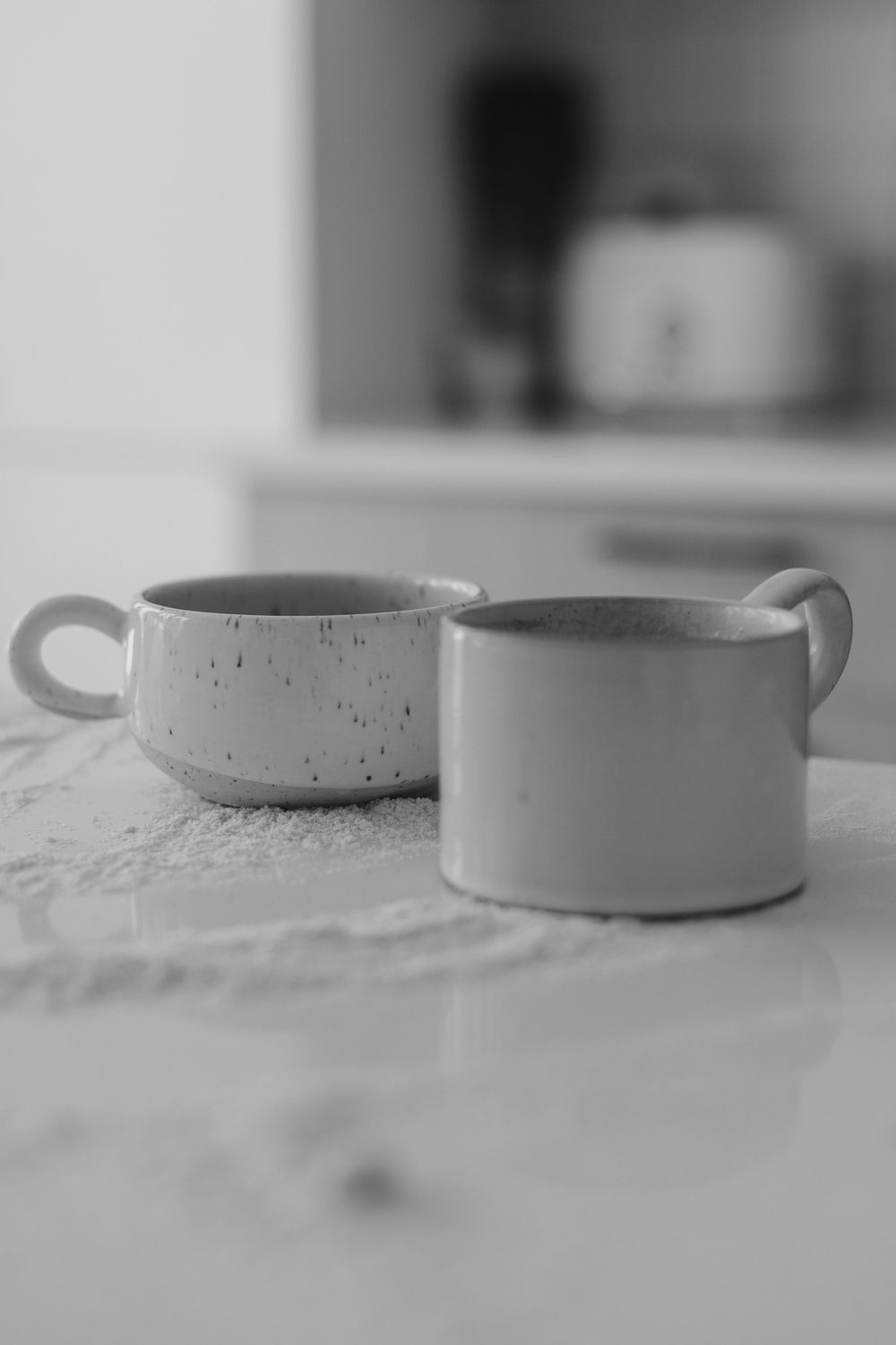 Minimalist black and white photograph of ceramic vessels arranged in a row on a textured surface.