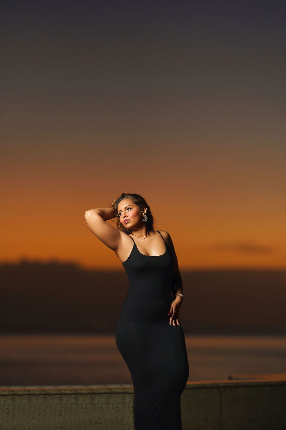 Silhouette of a dancer in a black dress striking elegant poses against a dramatic orange sunset sky.