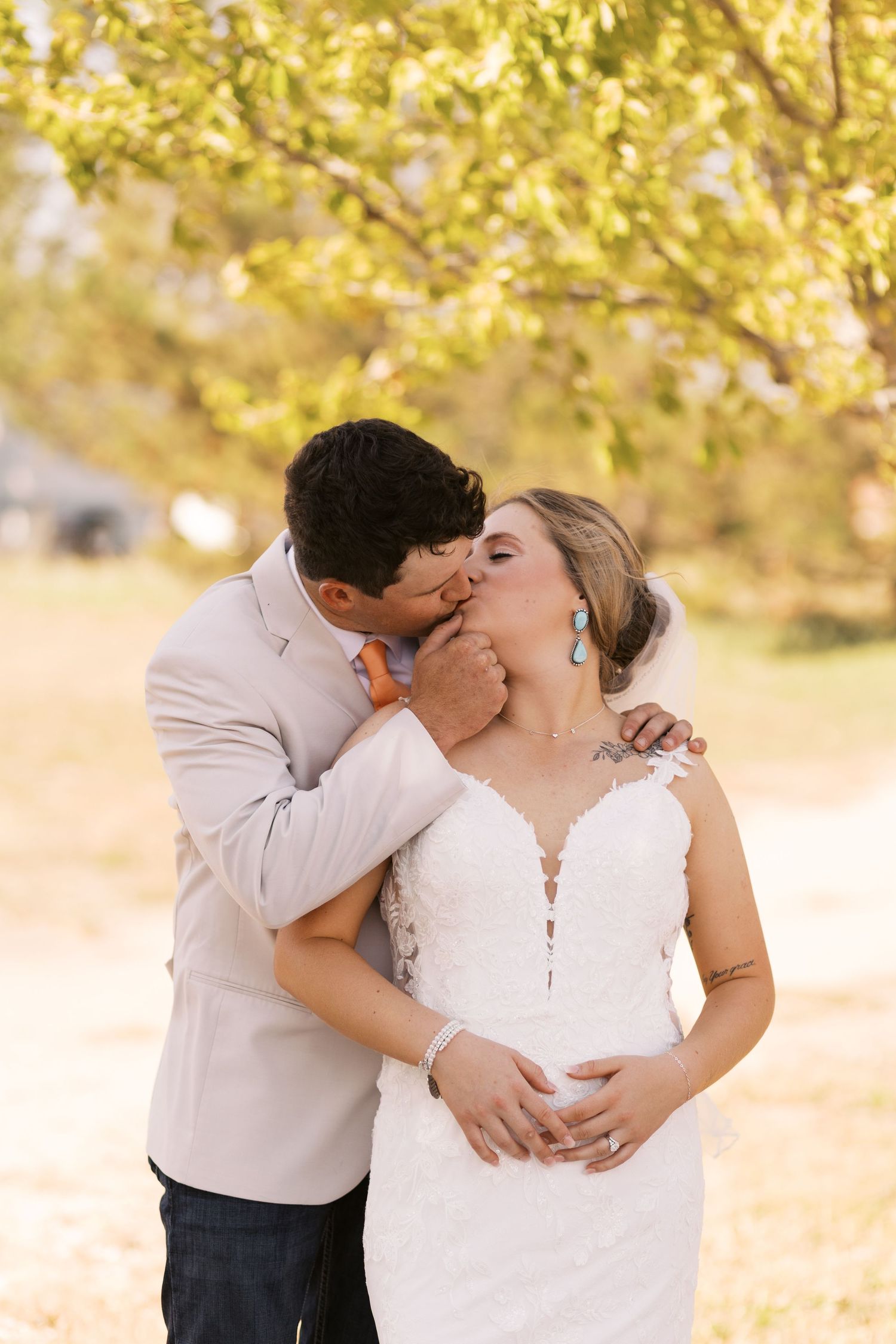 A romantic moment captured outdoors with a couple in white attire embracing under golden autumn foliage.