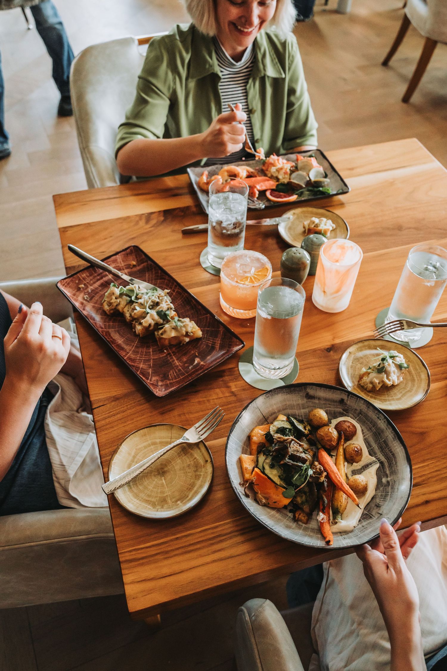 A wooden charcuterie board filled with meats, cheeses, bread, and pickled vegetables served with wine glasses.