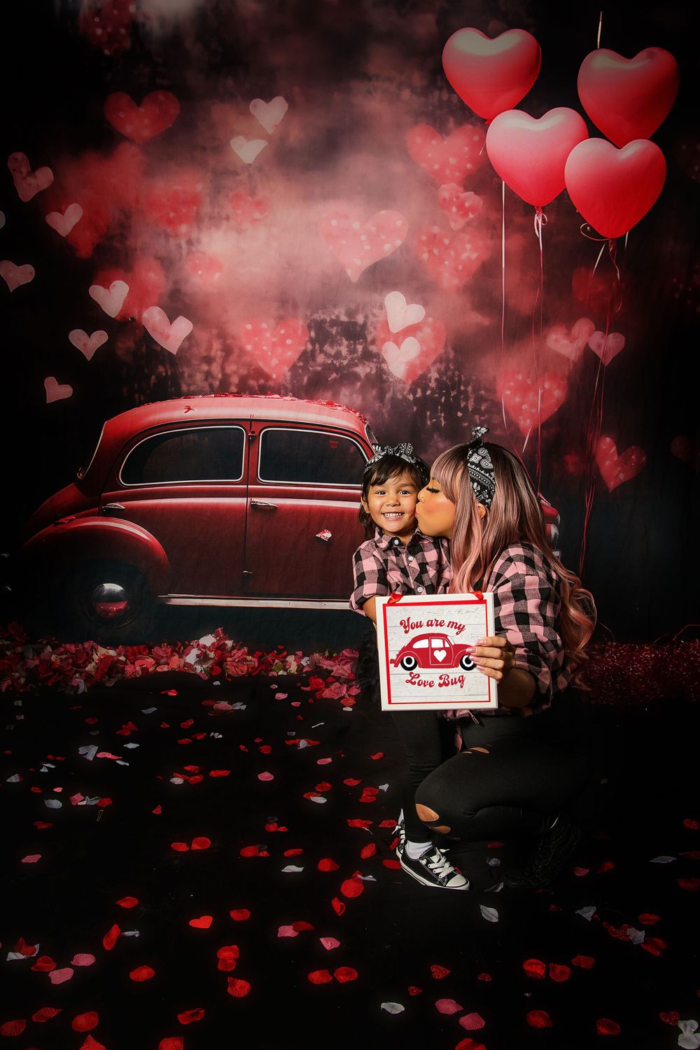 Valentine's day themed photo session with vintage red car against dark background with floating heart balloons and rose petals.