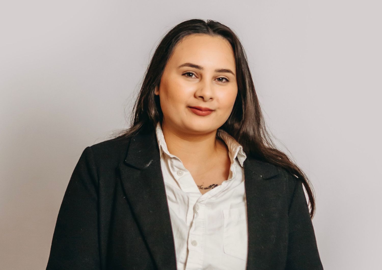 Professional headshot of person in black blazer and white blouse against light gray background.