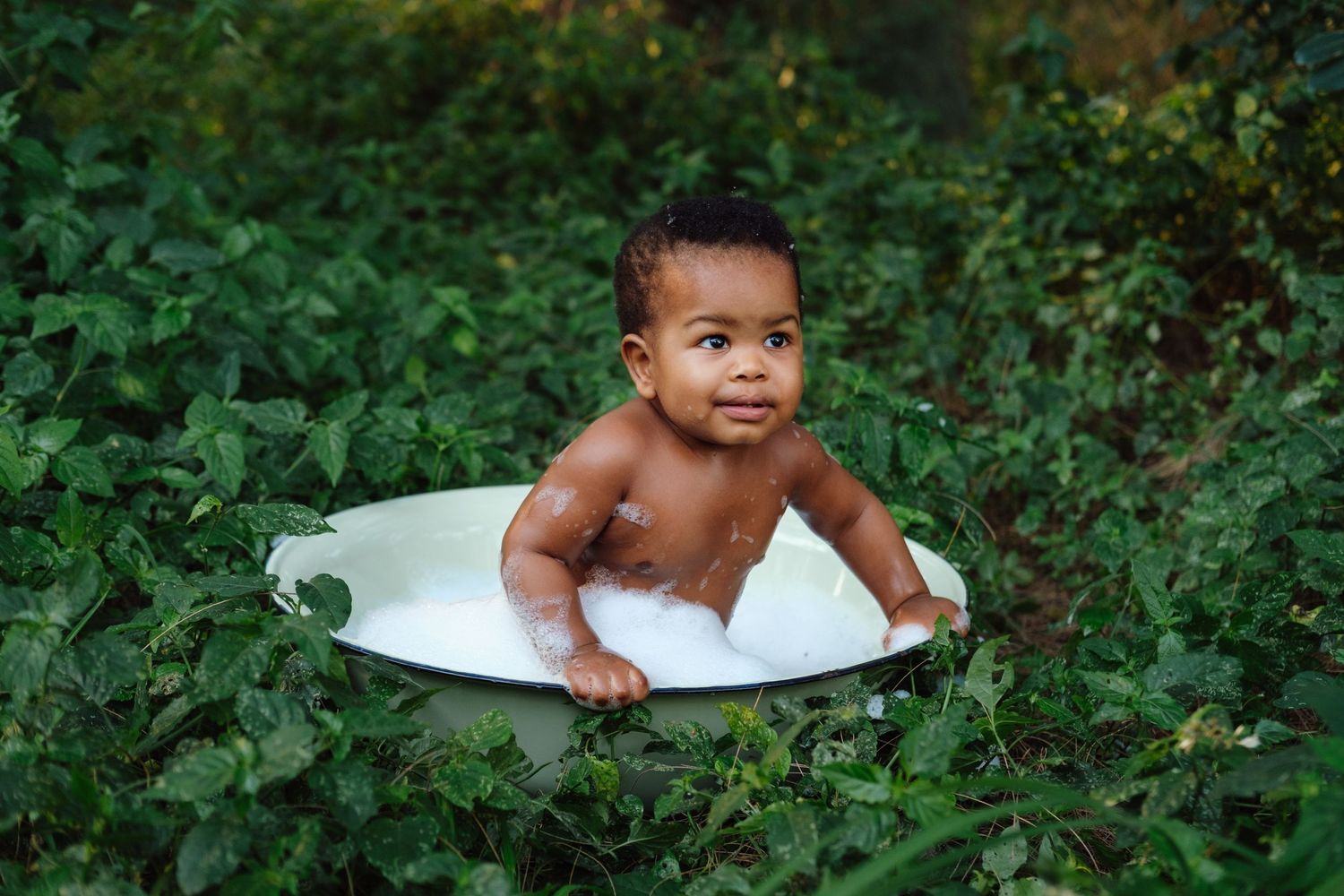 One-year-old boy sitting in a small bubble bath surrounded by plants