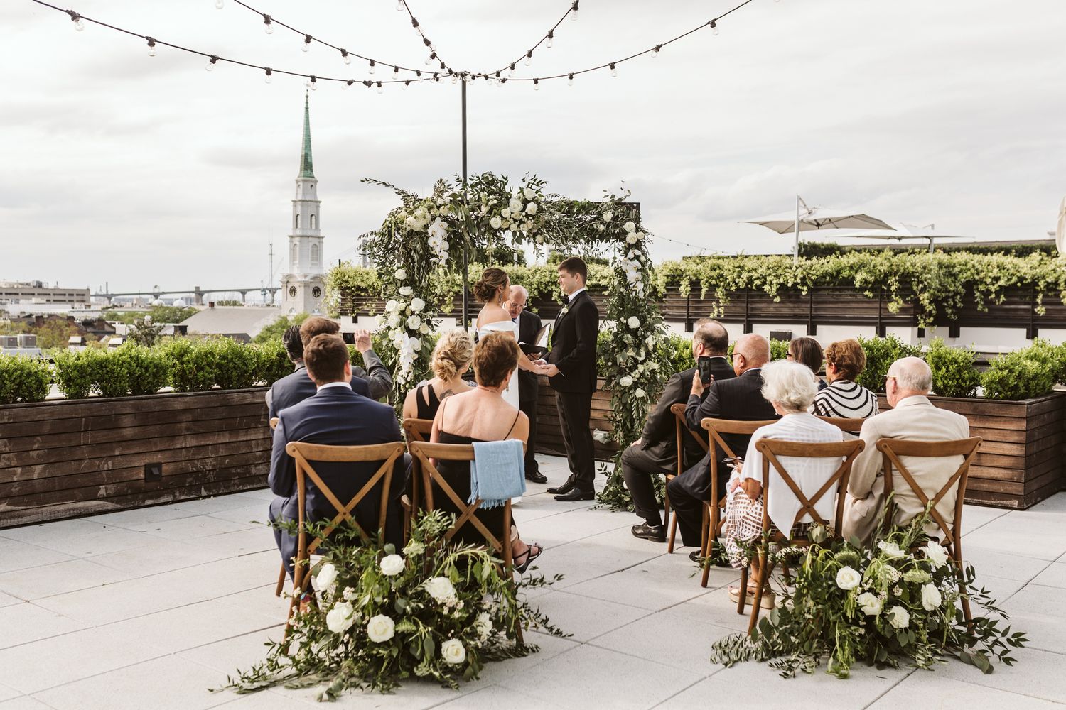 A bride and groom at their destination outdoor wedding in Savannah, GA, against a lush green hedge backdrop on the rooftop of Perry Lane.