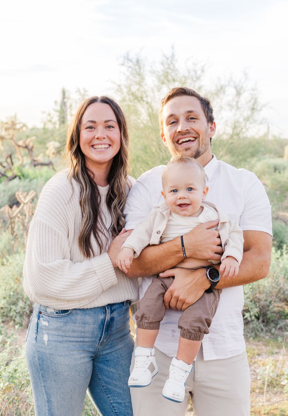 Light and airy family portrait of two parents and infant son smiling in a group hug in the Mesa, AZ desert.