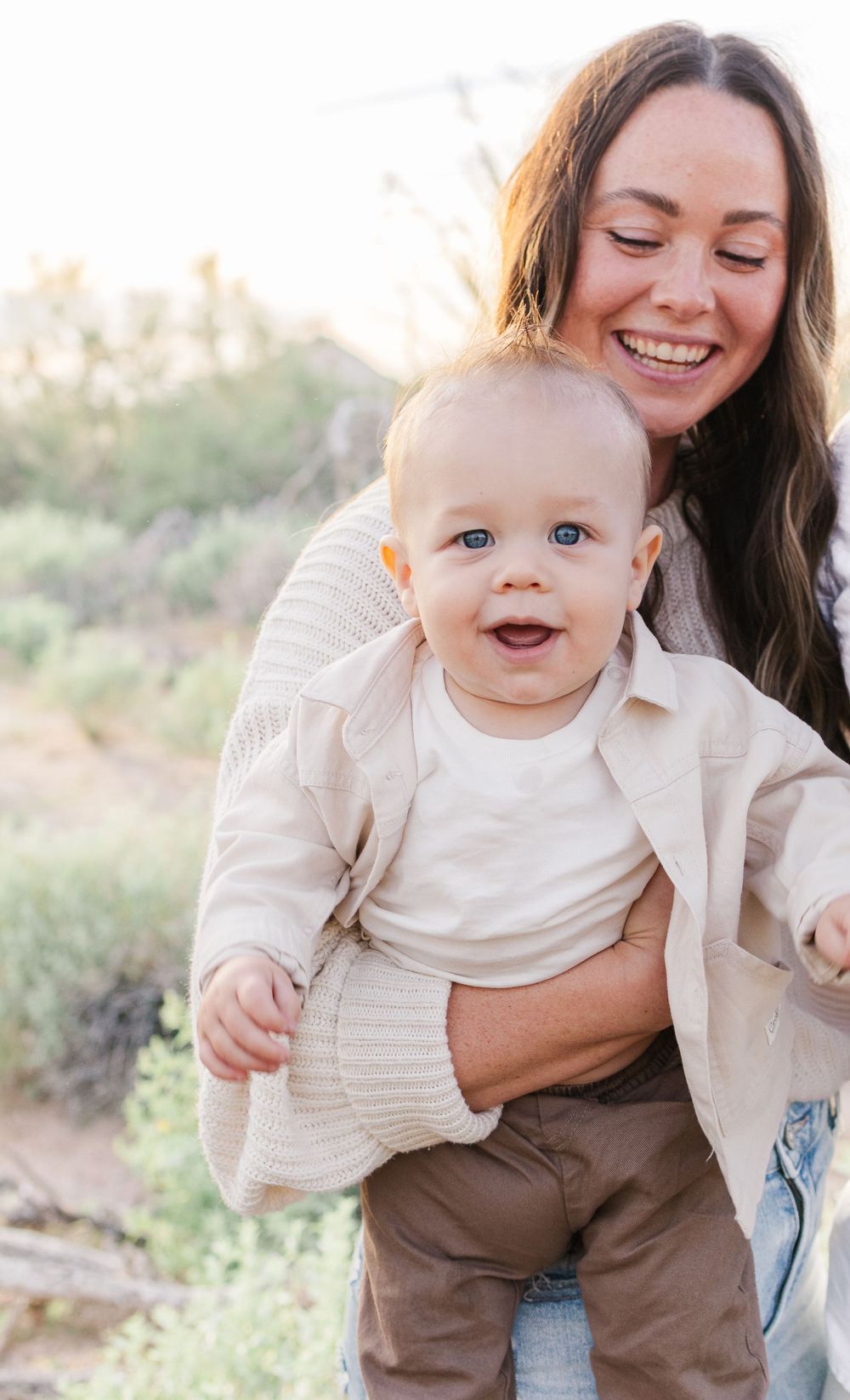 Light and airy family portrait of a young mom looking down at infant son smiling in the Arizona desert.