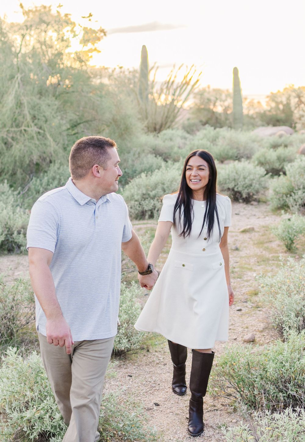 Light and airy portrait of a young married couple walking in the AZ desert with the man leading his wife and smiling back at her.