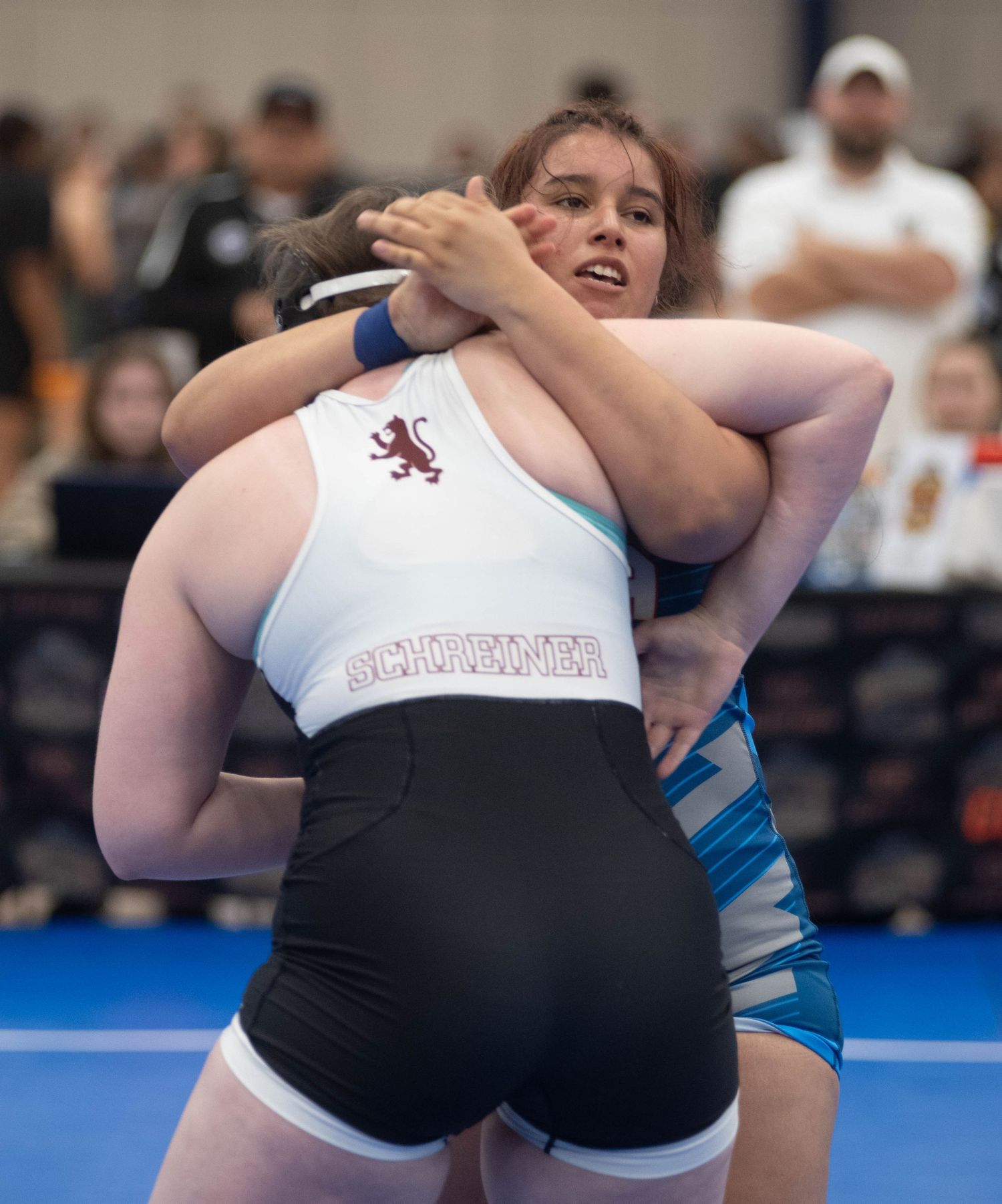 Two wrestlers in white and black uniforms competing during a match on blue mats.