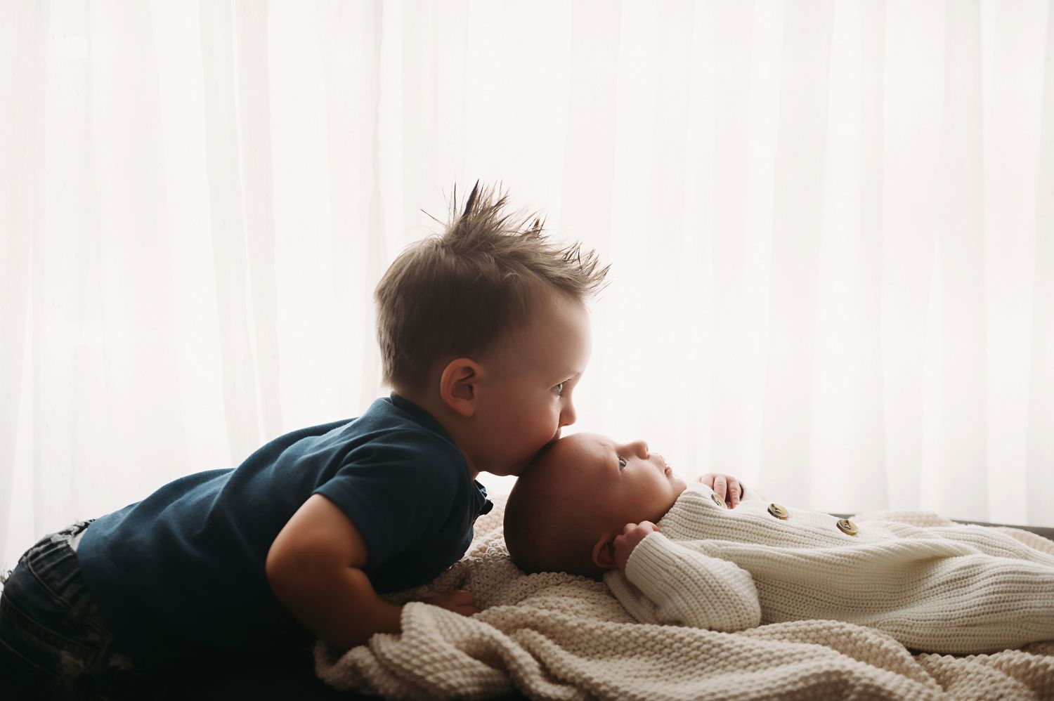 Toddler brother snuggling his new baby brother and giving him a kiss.