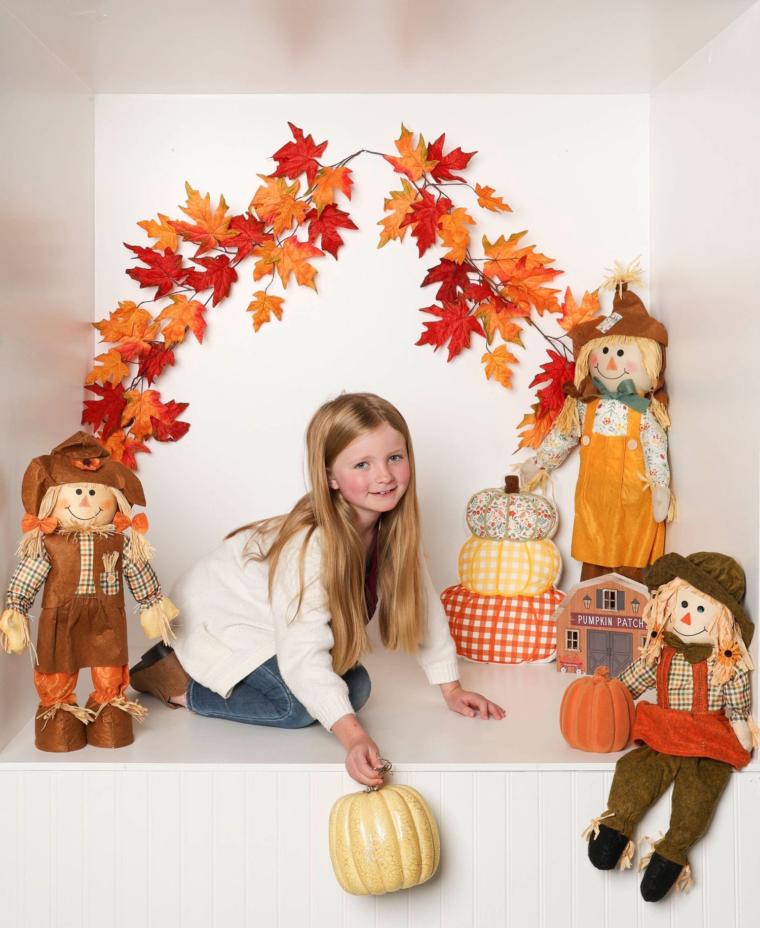 Fall themed photo setup with scarecrow dolls, orange maple leaf arch, and pumpkin decorations against white backdrop. Box photography