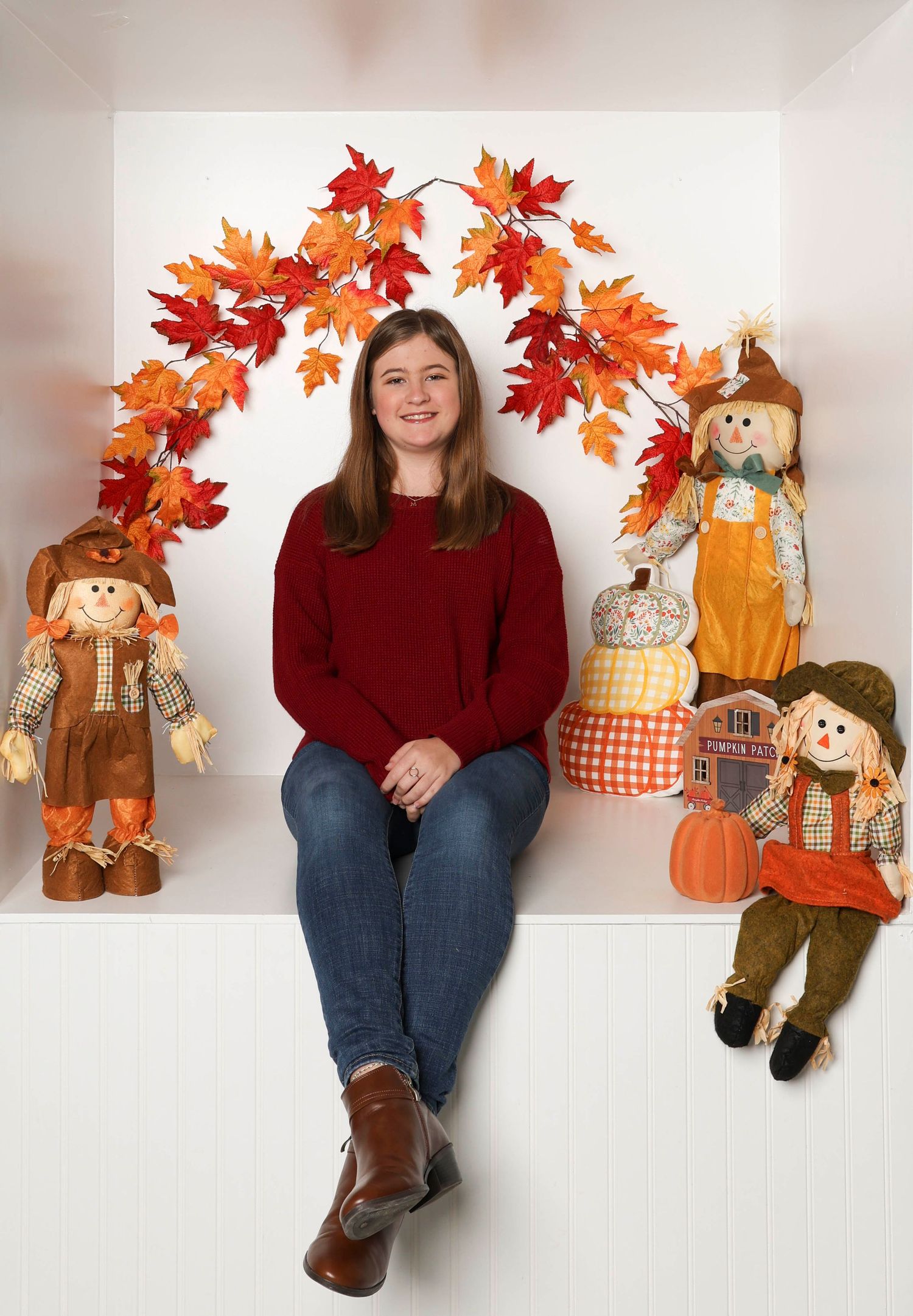 Autumn photo scene with burgundy sweater, scarecrows, maple leaf arch and pumpkin decorations. Box photography session