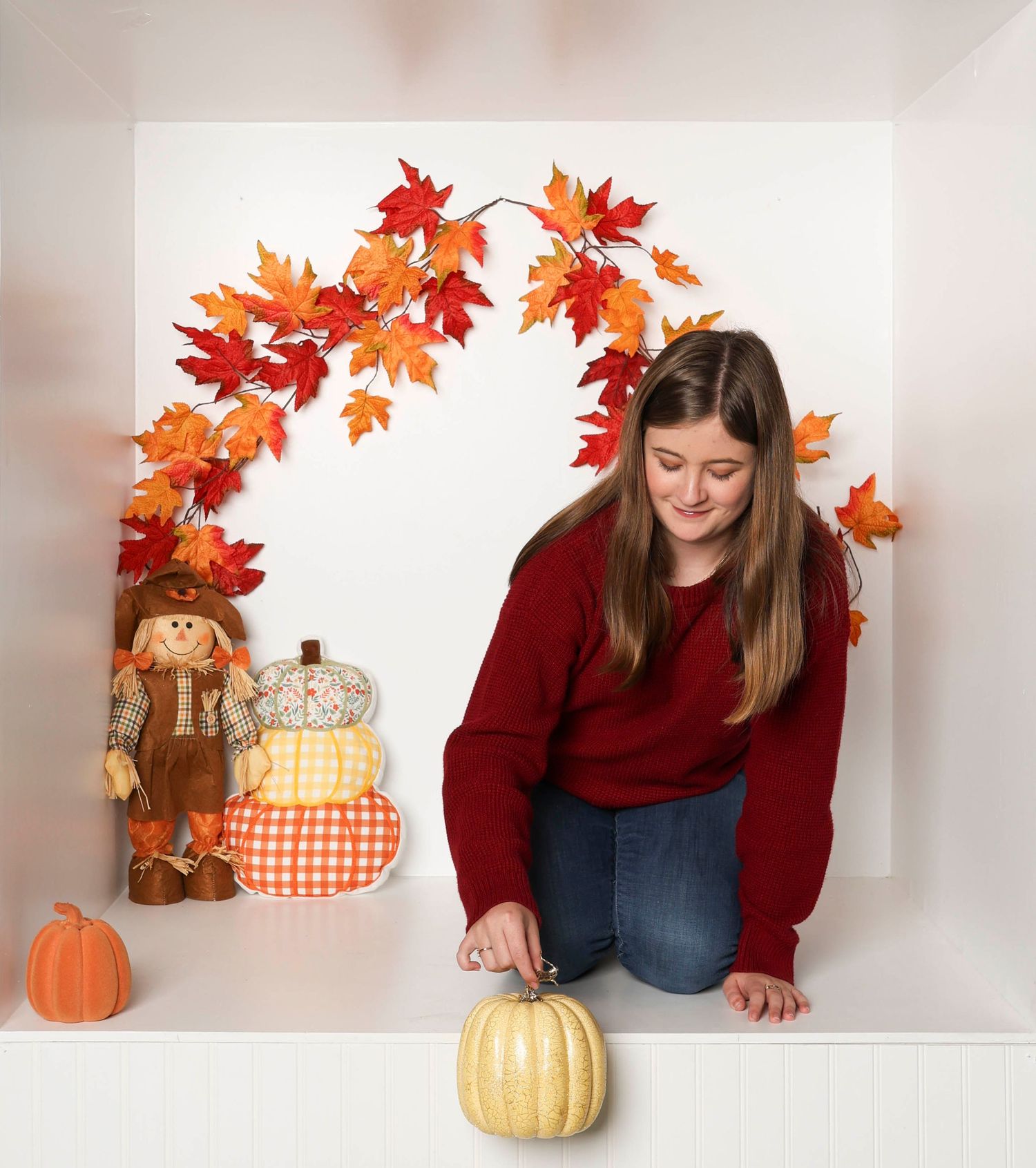 Seasonal autumn photo with burgundy sweater, decorative pumpkin, and maple leaf arch. Box photography session