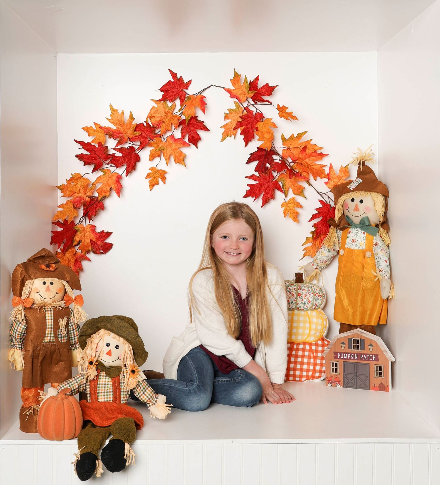 Cozy fall photo setup featuring scarecrow decorations, orange maple leaves, and pumpkin accents. Box photography session