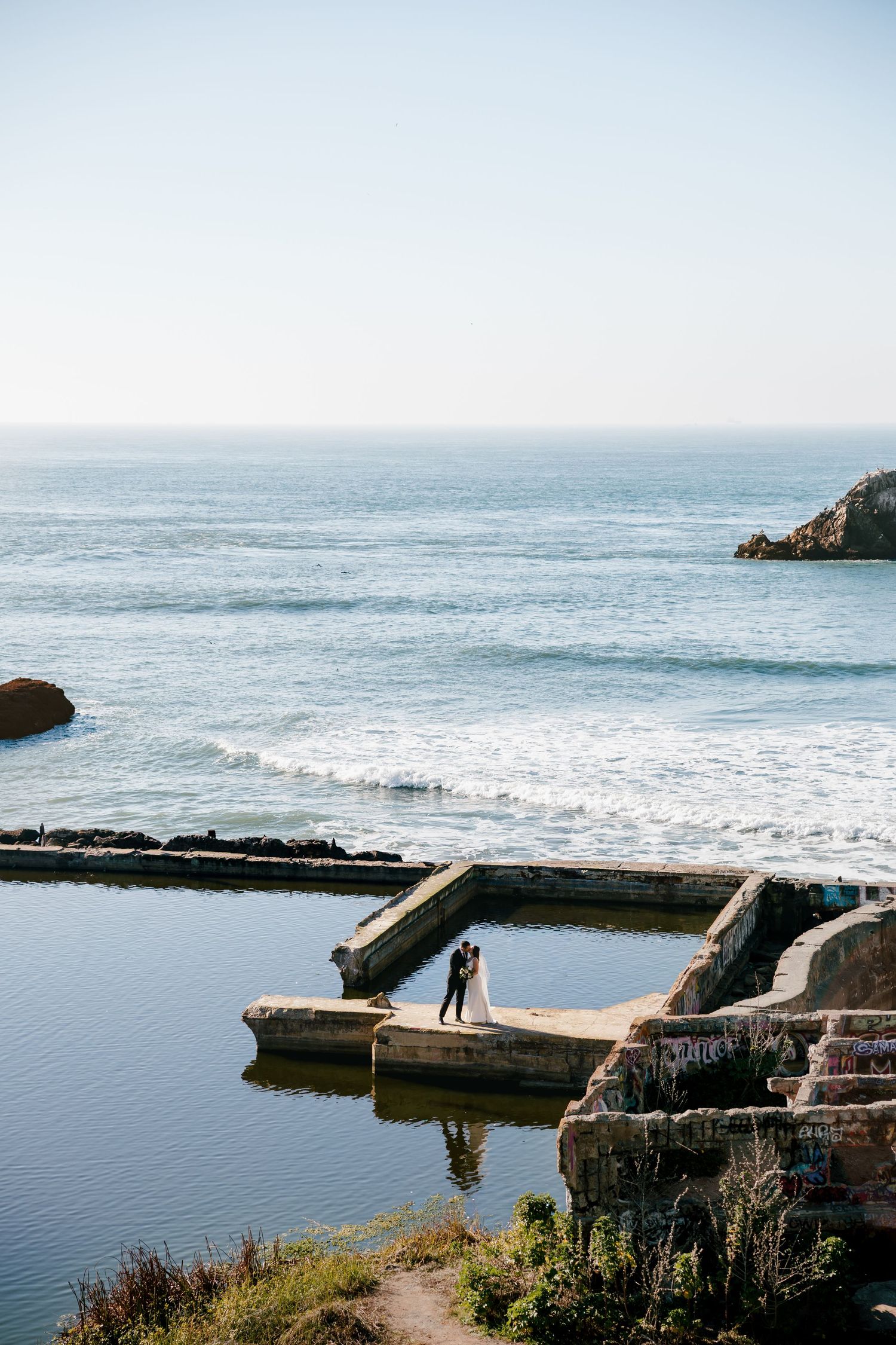 Wide shot of a coastal landscape featuring the historic Sutro Baths ruins with ocean waves crashing against rocky cliffs in San Francisco.
