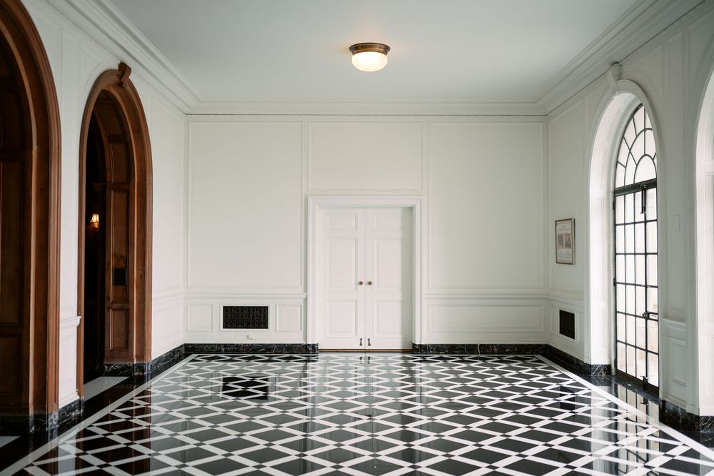Modern interior hallway with white walls, arched windows, and a striking black and white checkered floor pattern.