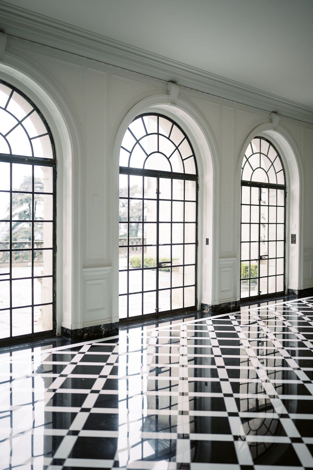 Black and white checkered floor in an elegant room with arched windows and white walls creates a dramatic optical illusion.