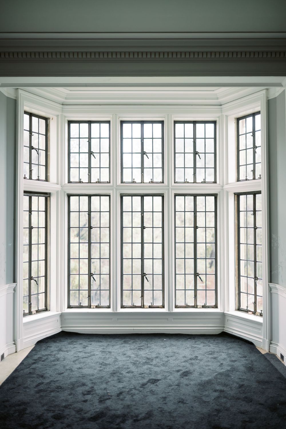 Modern sunroom with bay windows, white trim molding, and dark gray carpeting throughout.