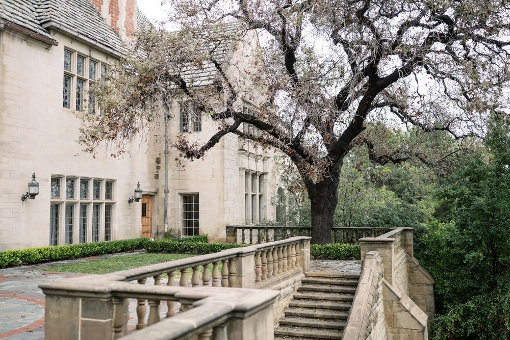 Elegant stone mansion with ornate balustrades and staircases surrounded by blooming trees in a formal garden setting.
