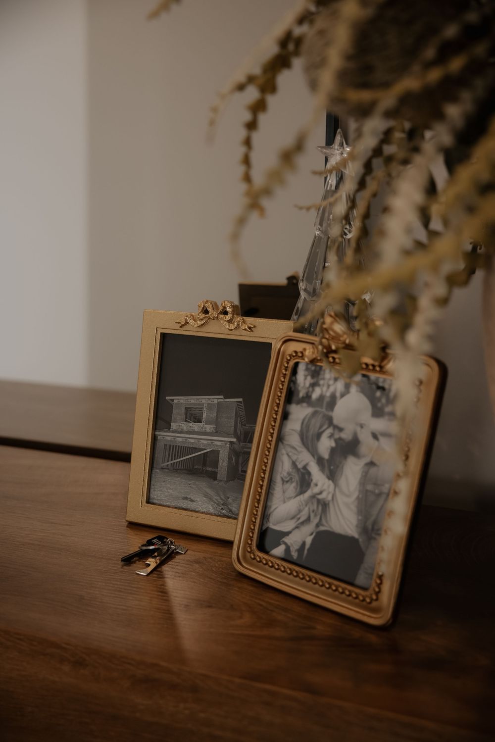 Vintage photographs in wooden frames displayed on dark wooden surface with dried flowers.