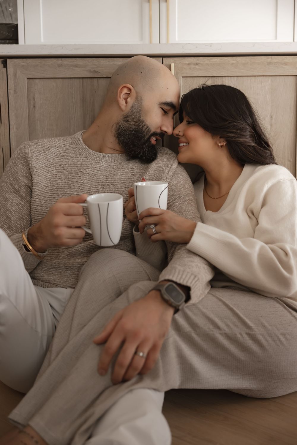 Couple relaxing on floor with coffee mugs in neutral colored outfits.