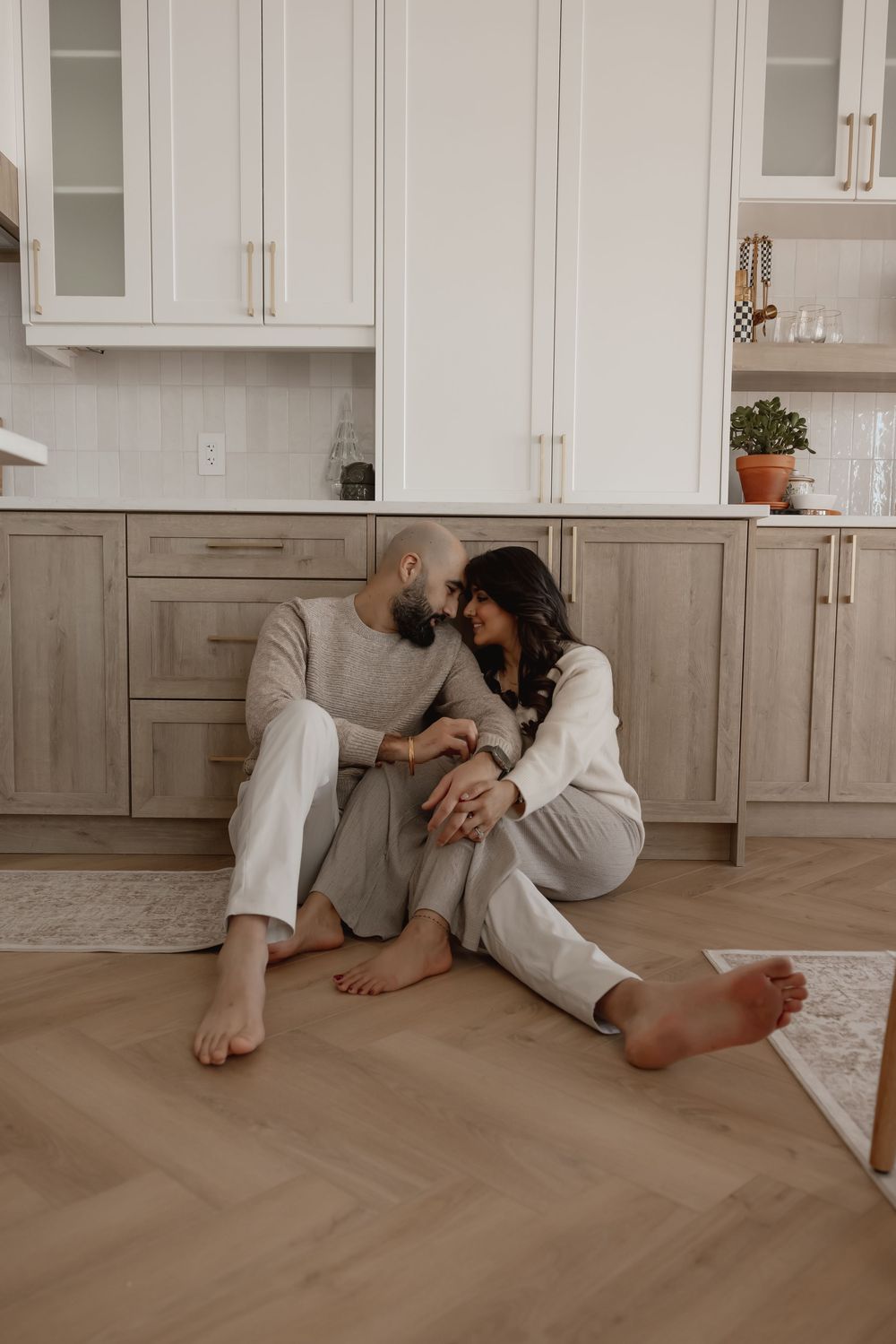 Romantic couple in matching loungewear laying on wooden floor in kitchen.