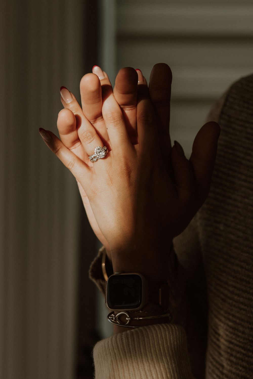 Close-up of intertwined hands with engagement ring in soft natural lighting.