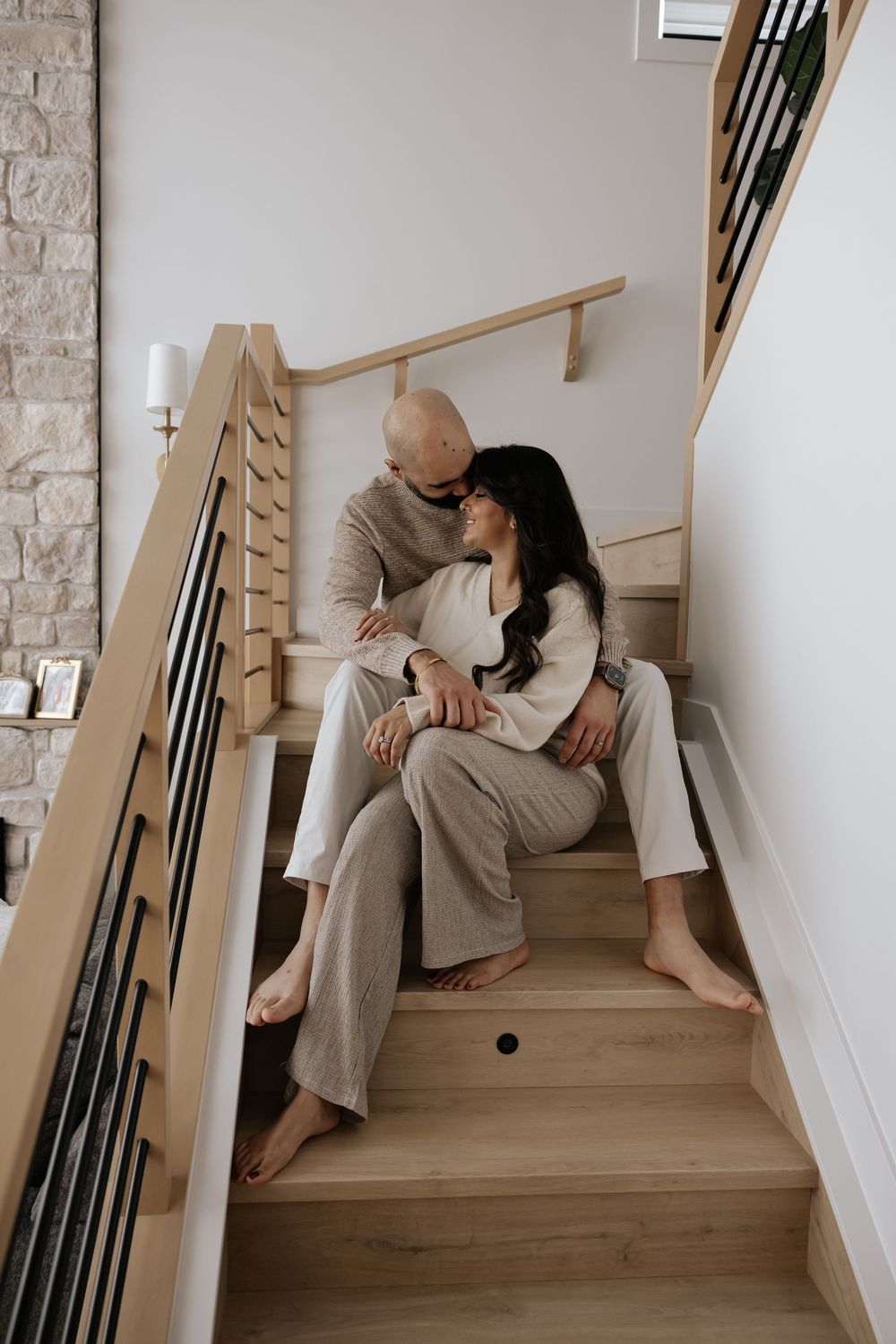 Couple sharing tender moments on wooden staircase in neutral toned clothing.