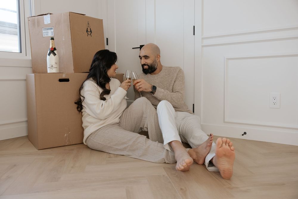 Couple relaxing on floor near moving boxes in bright white room.