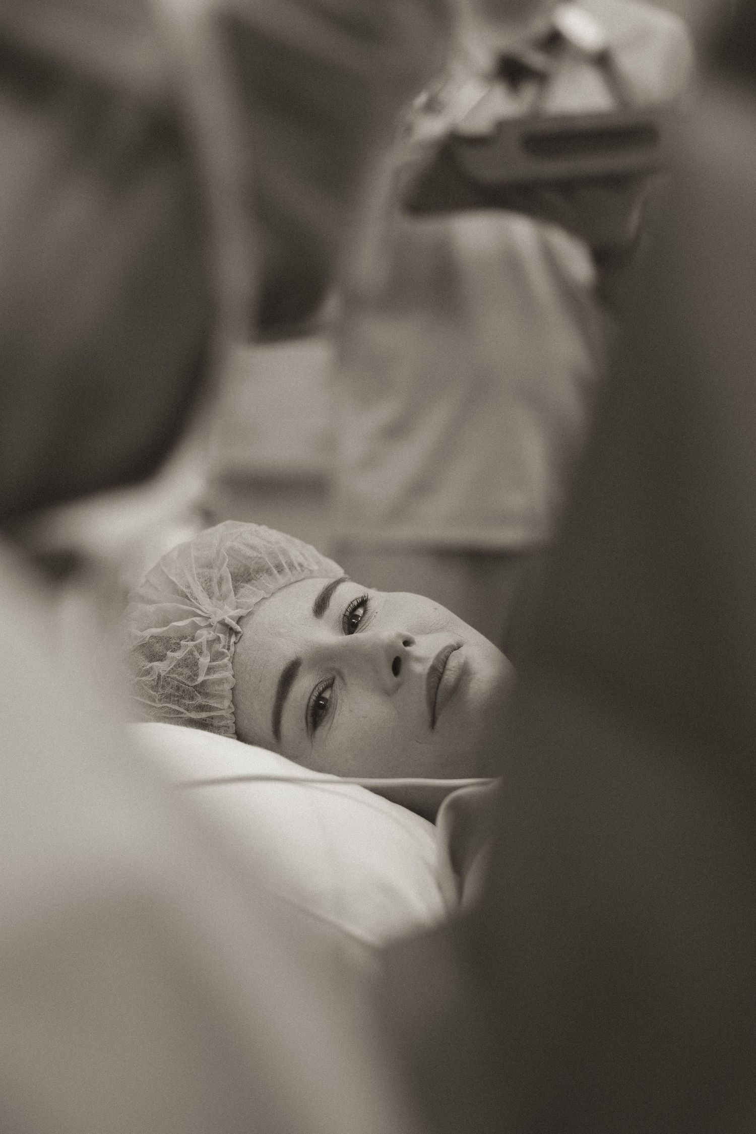 A black and white artistic portrait shows a person resting on white bedding with a soft, dreamy quality.