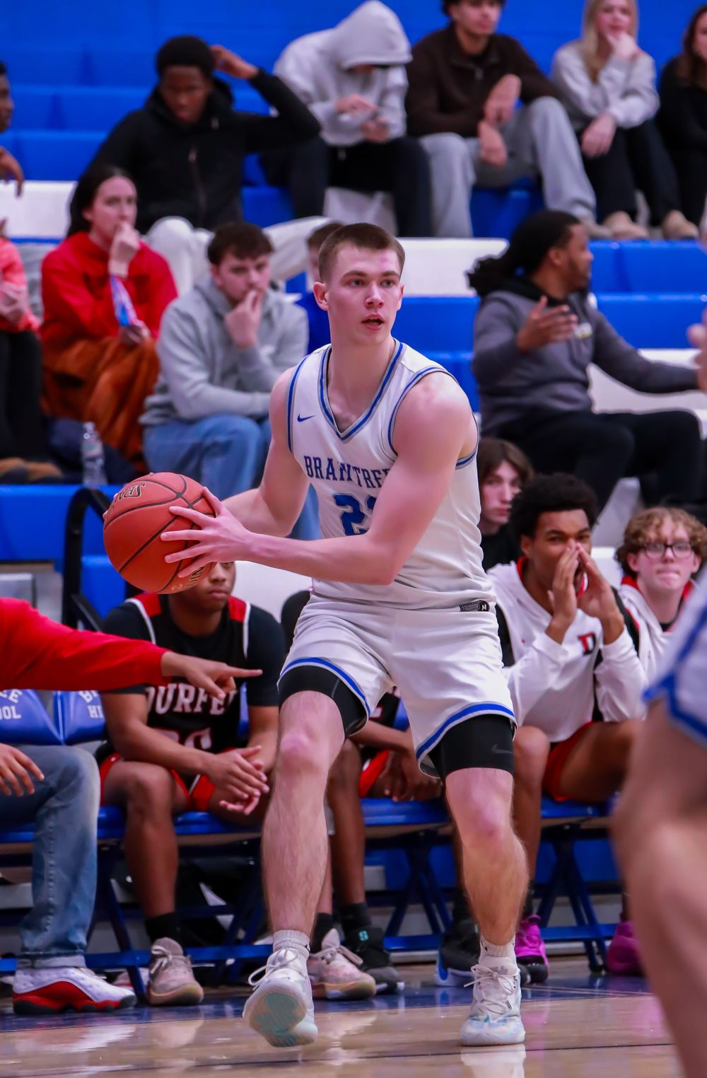 Basketball player in white jersey making defensive stance during game.