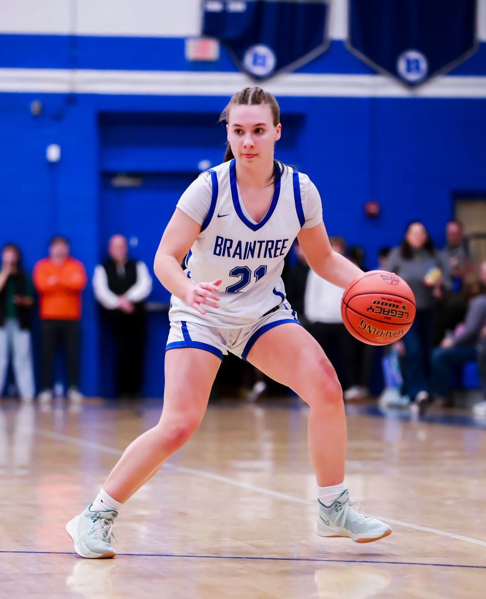 Basketball player in white uniform dribbles on blue court during game.