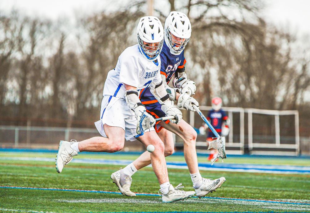 Lacrosse players battling for possession of the ball on a grass field.