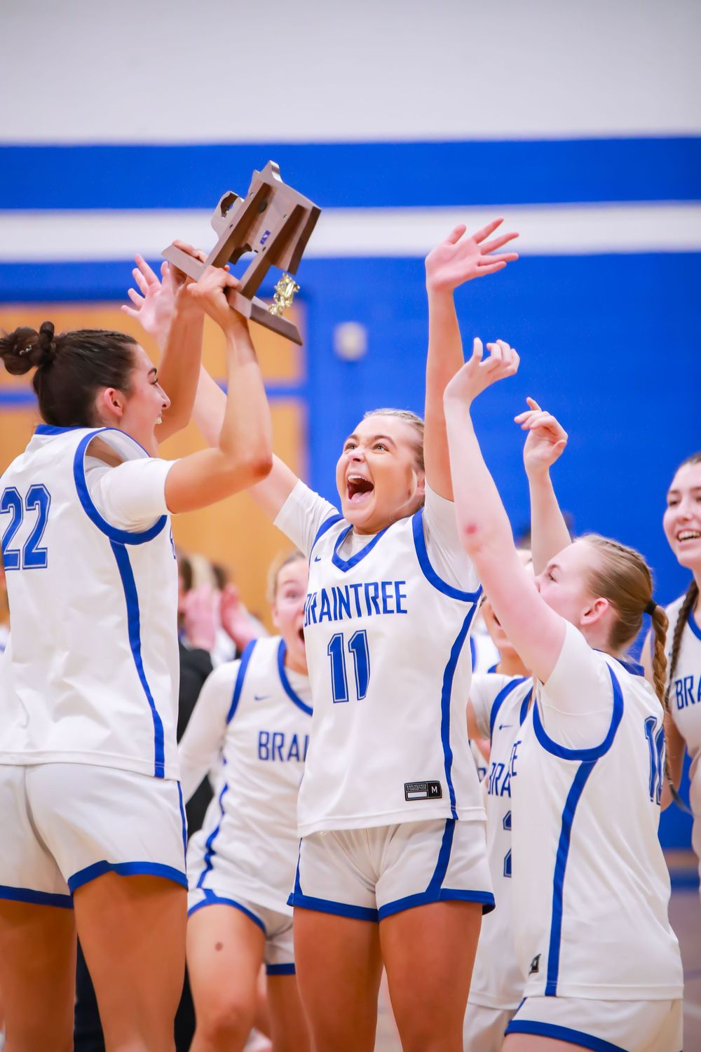 High school volleyball team celebrating victory in blue and white uniforms.