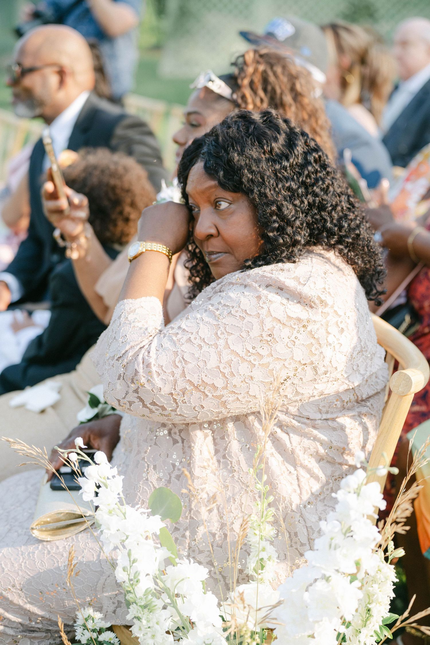 Wedding guest in delicate lace dress sits among white floral decorations at outdoor ceremony. - Elawa Farm