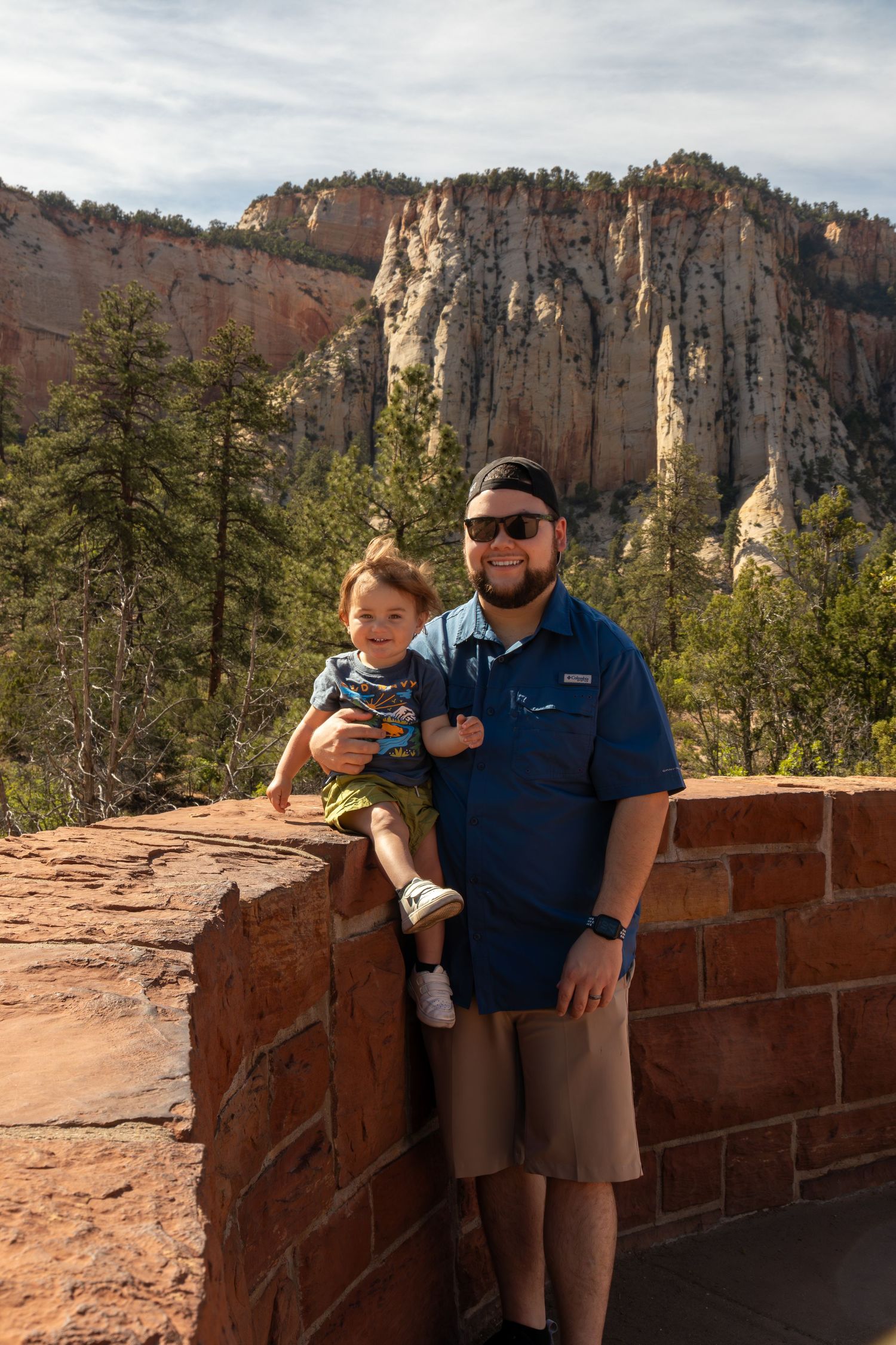 Visitors enjoy scenic view of towering red rock cliffs at Zion National Park from stone observation area.