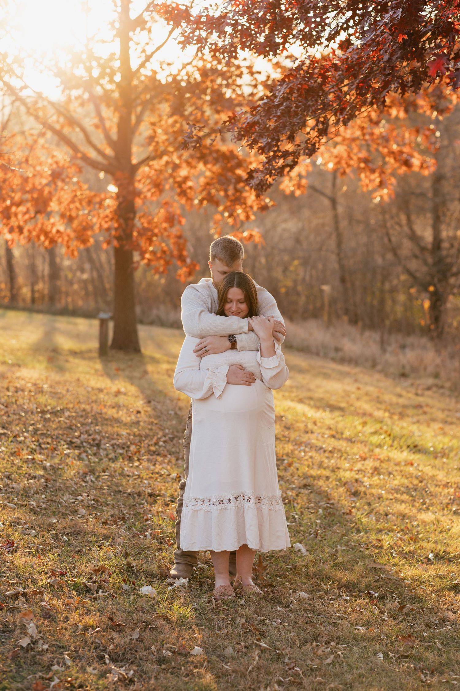 Loving embrace in autumn forest during golden hour maternity session.