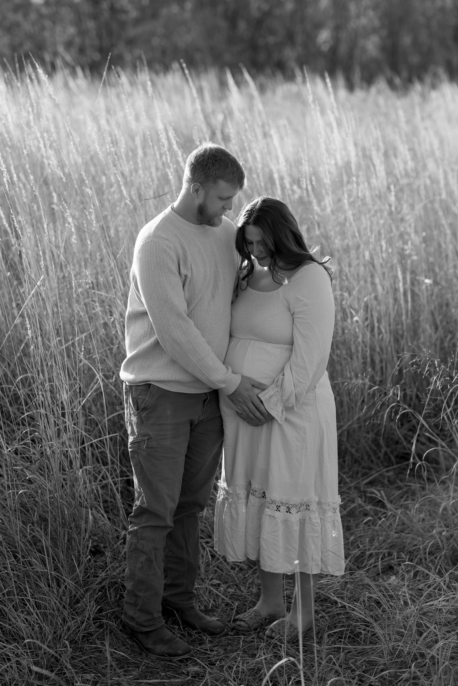 Black and white portrait of a couple embracing in a tall grass field.