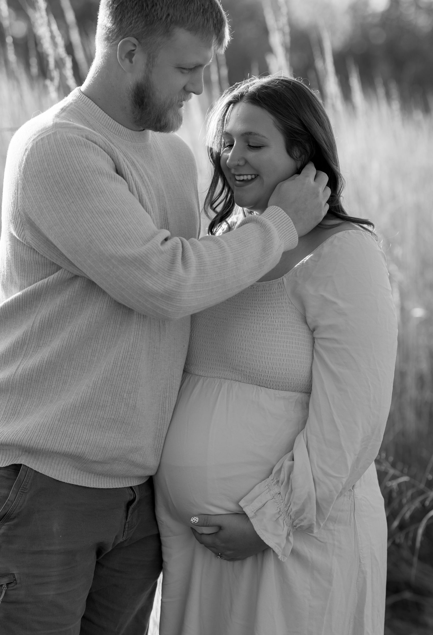 Black and white intimate maternity portrait showing couple sharing a tender moment in tall grass.