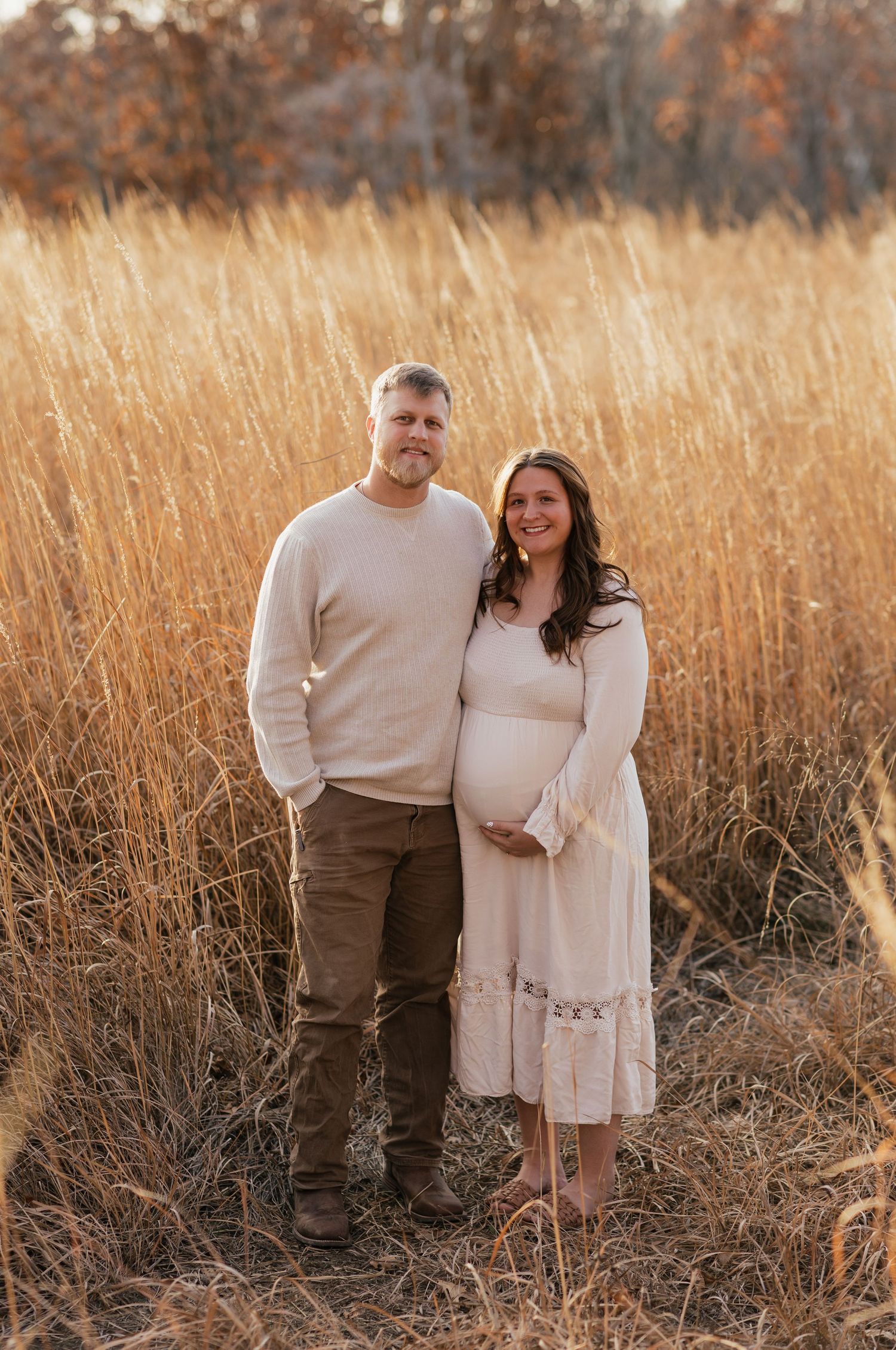 Couple in neutral tones standing together in a golden autumn field at sunset.