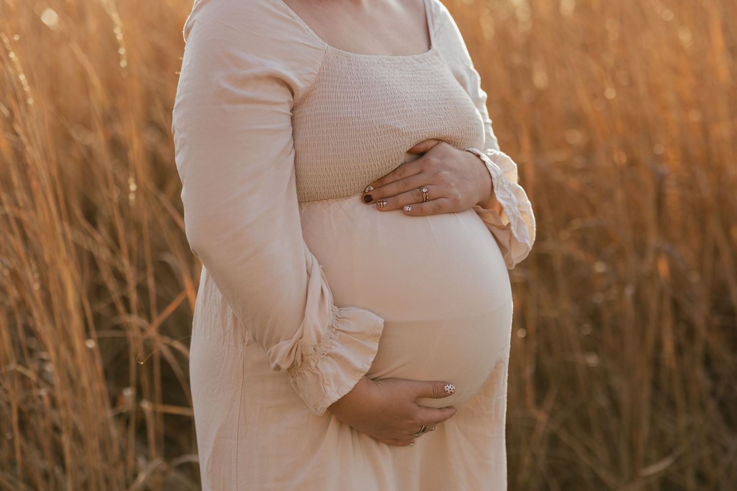 Close-up of pregnant belly in white dress during golden hour maternity photoshoot.