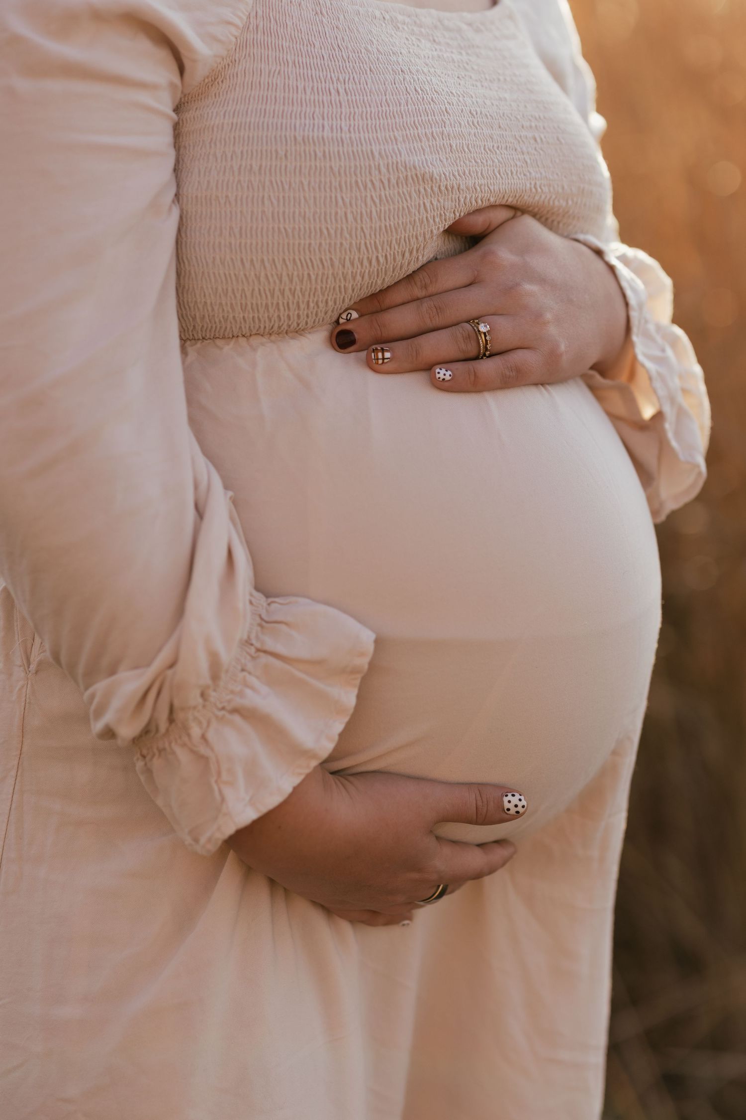 Detail shot of hands cradling pregnant belly, showing wedding ring against white dress.