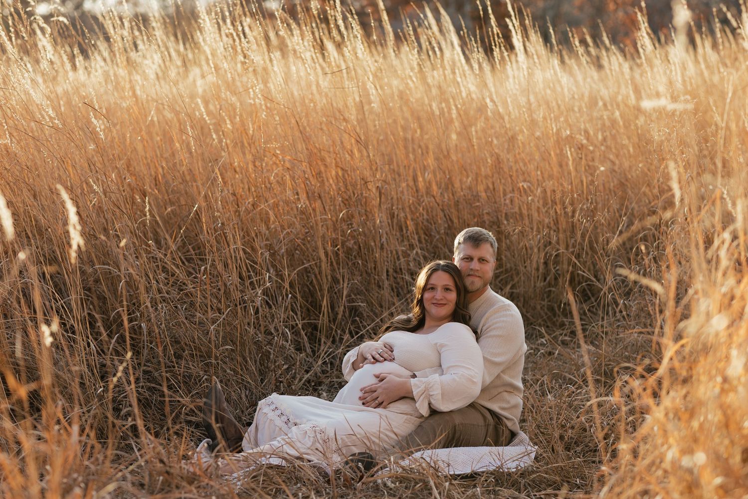 Couple relaxing together in tall autumn grass during sunset maternity session.