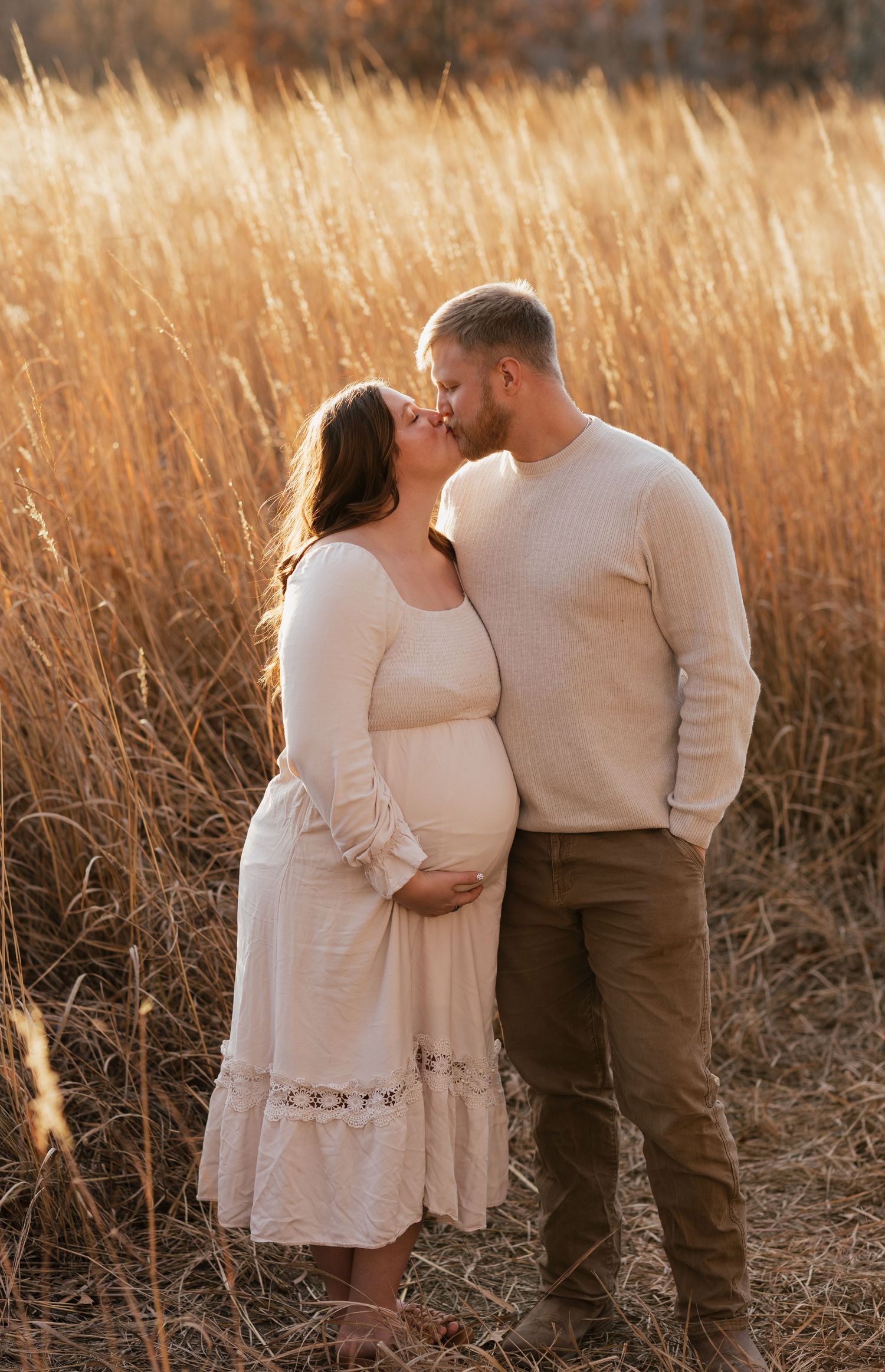 A romantic maternity photoshoot in a golden wheat field during sunset shows an intimate moment between a couple.