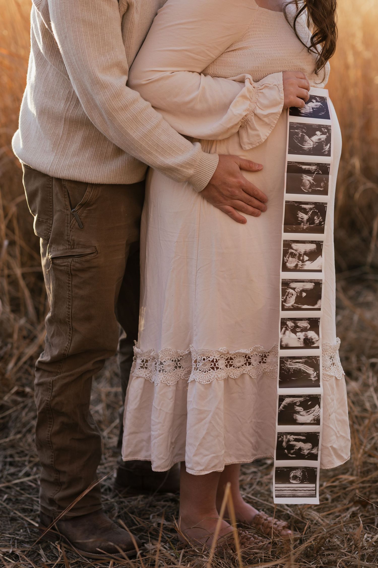 Close-up of ultrasound strip held against a cream dress during an outdoor maternity photoshoot.