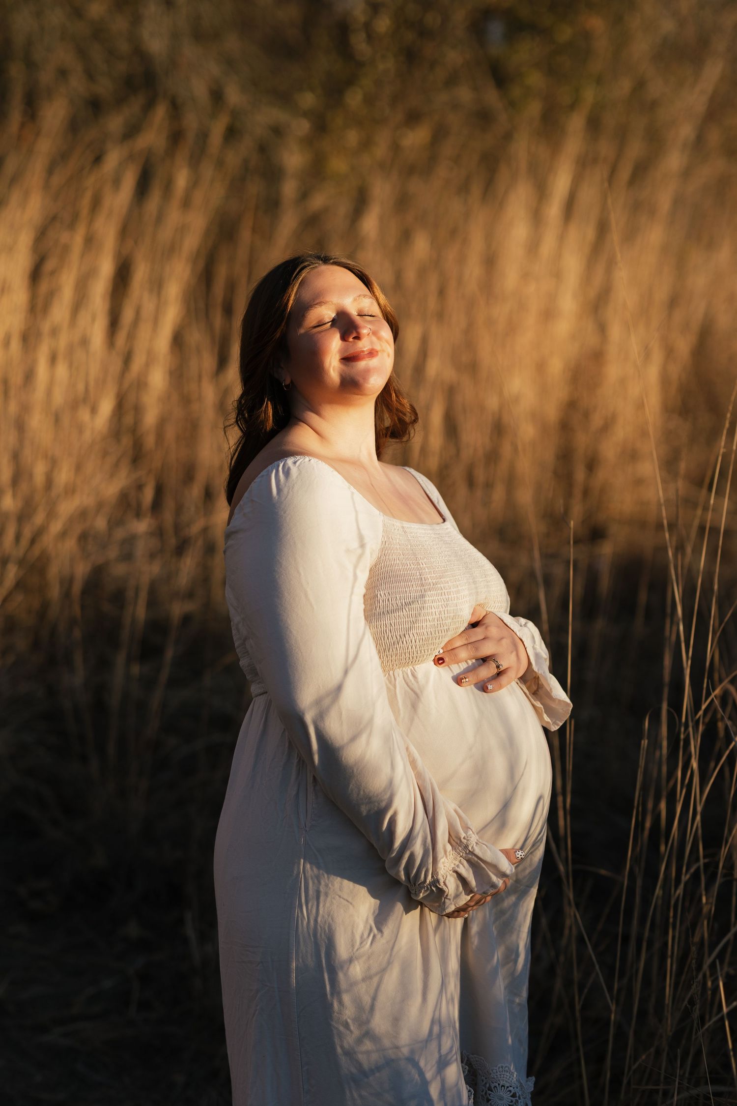 Side profile maternity portrait with dramatic lighting and golden grass backdrop.