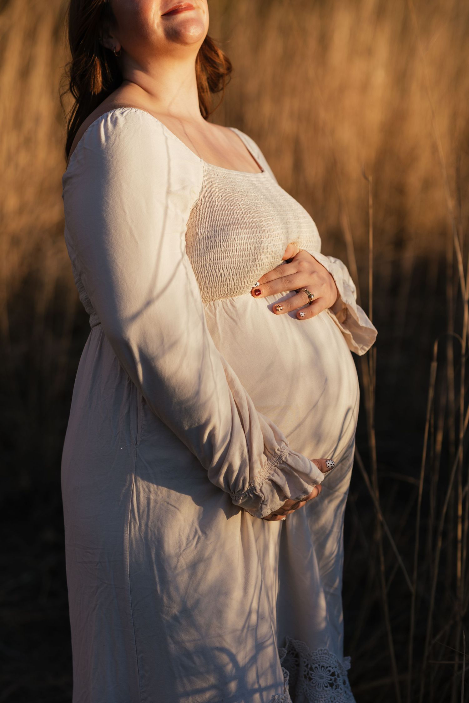 Close-up maternity photo showing belly in white dress against warm autumn backdrop.