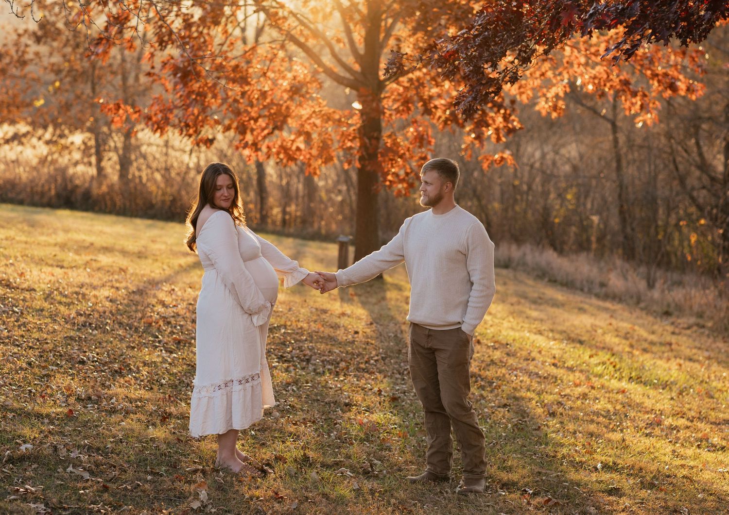 Couple embraces in a golden autumn field during sunset maternity photoshoot.