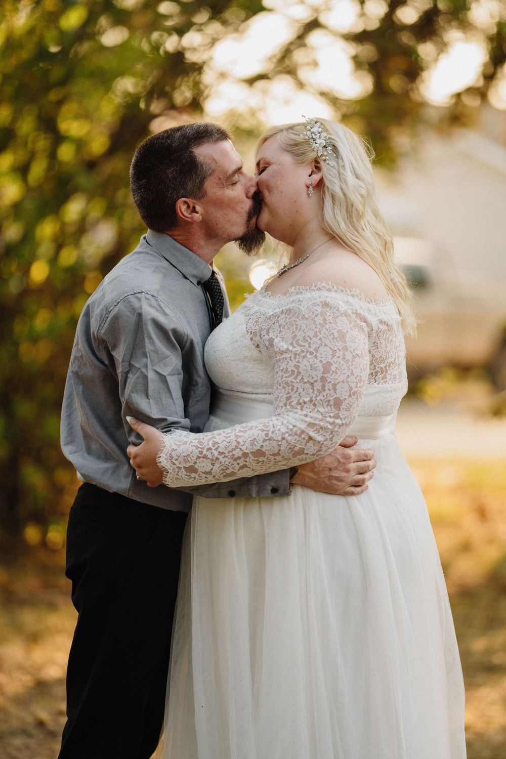 Bride and groom share a passionate kiss outdoors with golden autumn foliage in the background.